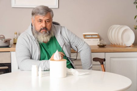Porträt eines traurigen älteren Mannes mit Taschentüchern, der in der Küche am Tisch sitzt