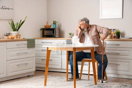 Porträt eines traurigen älteren Mannes mit Taschentüchern, der in der Küche am Tisch sitzt