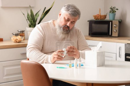 Porträt eines traurigen älteren Mannes, der mit Taschentüchern und Medikamenten in der Küche am Tisch sitzt
