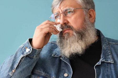 Photo for Portrait of sad senior man with tissues wiping eyes on blue background, closeup - Royalty Free Image