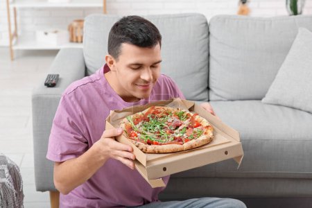 Photo for Young man holding cardboard box with tasty pizza at home - Royalty Free Image