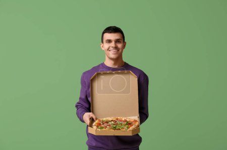 Photo for Happy young man holding cardboard box with tasty pizza on green background - Royalty Free Image