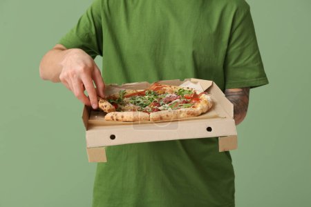 Photo for Young man holding cardboard box with tasty pizza on green background - Royalty Free Image