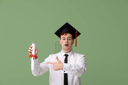 Photo for Male student in mortar board pointing at diploma on green background - Royalty Free Image