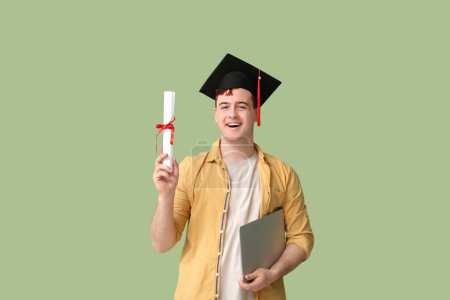 Photo for Male student in mortar board with diploma and modern laptop on green background - Royalty Free Image
