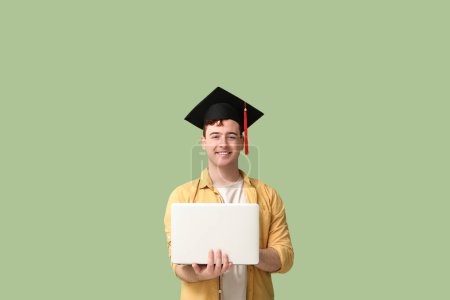 Photo for Male student in mortar board with modern laptop on green background - Royalty Free Image
