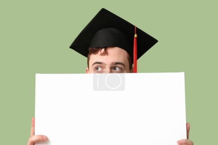 Photo for Male student in mortar board with blank poster on green background - Royalty Free Image