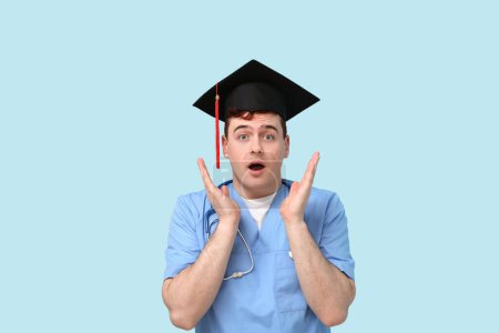Photo for Shocked male student in mortar board and uniform of doctor on blue background - Royalty Free Image