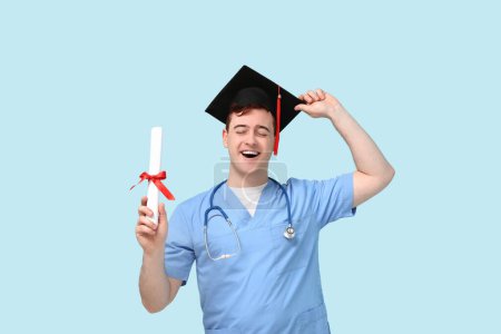 Photo for Male student in mortar board and uniform of doctor with diploma on blue background - Royalty Free Image