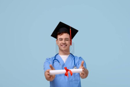 Photo for Male student in mortar board and uniform of doctor with diploma on blue background - Royalty Free Image