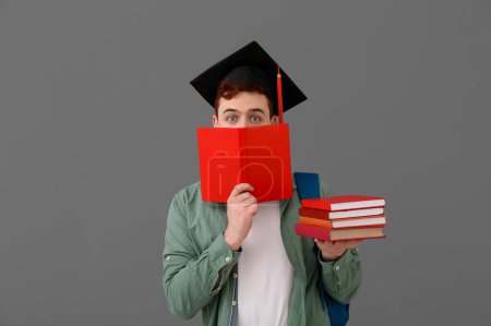 Photo for Male student in mortar board with books and backpack on grey background - Royalty Free Image