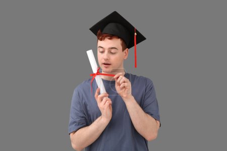 Photo for Male student in mortar board with diploma on grey background - Royalty Free Image