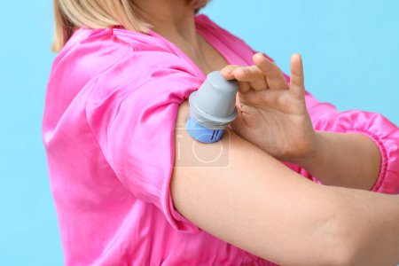 Frau mit Glukosesensor zur Messung des Blutzuckerspiegels und Applikator auf blauem Hintergrund, Nahaufnahme. Diabetes-Konzept