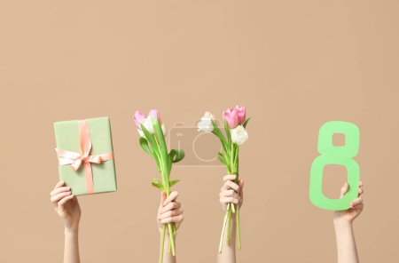 Weibliche Hände mit Papierfigur 8, Geschenkschachtel und Tulpenblumen zum Internationalen Frauentag auf farbigem Hintergrund