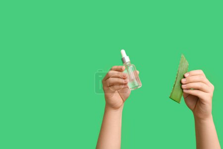 Female hands with bottle of cuticle oil and aloe vera on green background