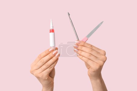 Female hands with cuticle oil pen, pusher and nail file on pink background