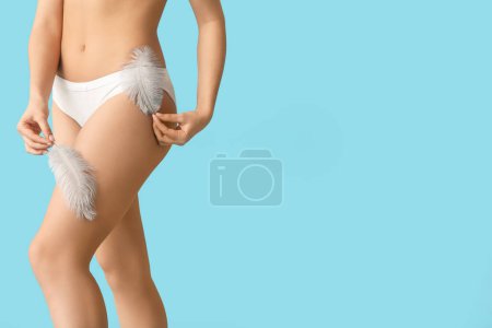 Young woman with soft feathers on blue background. Epilation concept