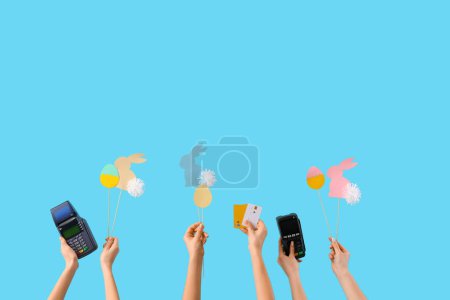 Women with payment terminals, credit cards and Easter decor on blue background. Online shopping