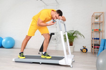 Sporty young man using inhaler on treadmill in gym