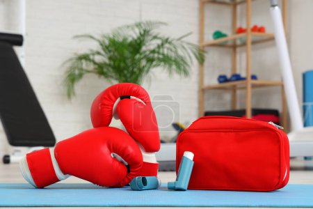 Téléchargez les photos : Inhalateurs d'asthme avec gants de boxe et trousse de premiers soins sur tapis dans la salle de gym, gros plan - en image libre de droit