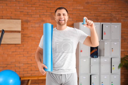 Sporty young man with fitness mat and inhaler in gym