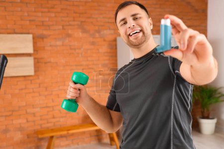Sporty young man with inhaler and dumbbell in gym