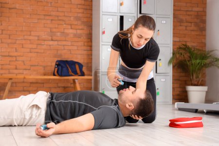 Female trainer with inhaler giving man first aid in gym