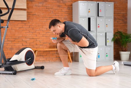 Sporty young man with inhaler having asthma attack in gym