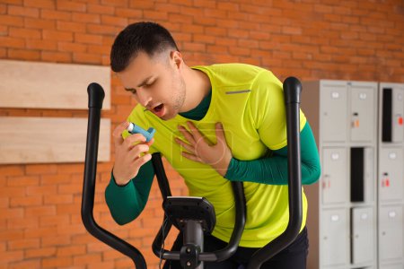 Jeune homme sportif utilisant inhalateur sur vélo d'exercice dans la salle de gym