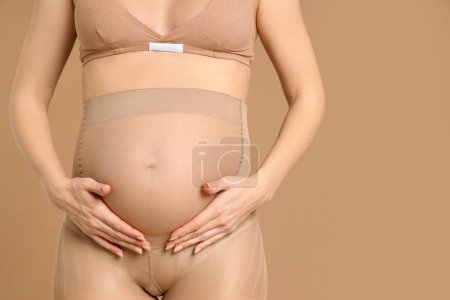 Young pregnant woman in tights on beige background, closeup