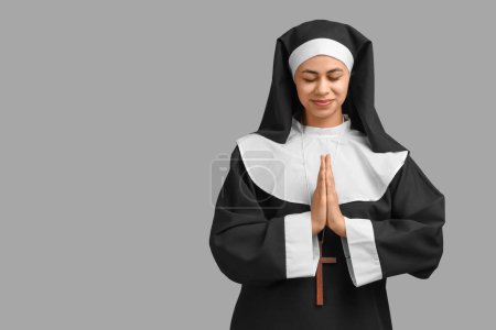 Portrait of young praying nun on grey background