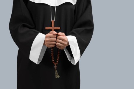 Young nun with rosary beads on grey background, closeup