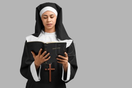 Portrait of young nun reading Bible on grey background