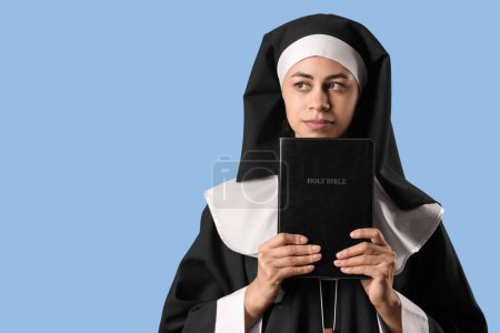 Young nun with Bible on blue background