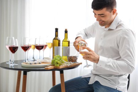 Téléchargez les photos : Jeune sommelier verser du vin dans le verre dans la cuisine - en image libre de droit