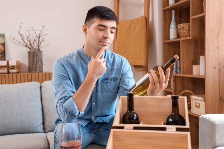 Téléchargez les photos : Jeune homme réfléchi avec bouteille de vin à la maison - en image libre de droit