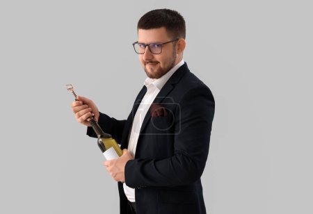 Photo for Young sommelier opening bottle of wine on grey background - Royalty Free Image