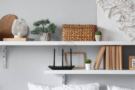 Modern wi-fi router with books and plants on hanging shelves in room