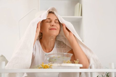 Photo for Mature woman with towel doing steam inhalation in bedroom - Royalty Free Image