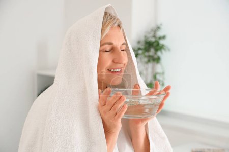 Mature woman with towel doing steam inhalation in bedroom, closeup