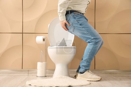 Junger Mann mit Hämorrhoiden und Daumen auf Toilettenschüssel in Toilette