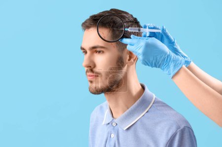 Young brunette man receiving injection for hair growth on blue background, closeup