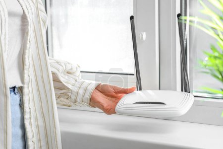 Woman with wi-fi router near window at home, closeup