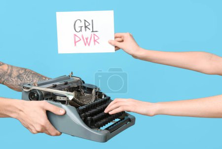 Manos sosteniendo una máquina de escribir vintage y una postal festiva con texto GRL PWR sobre fondo azul. Celebración del Día de la Mujer