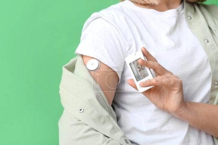 Woman with glucose sensor and glucometer on green background, closeup. Diabetes concept