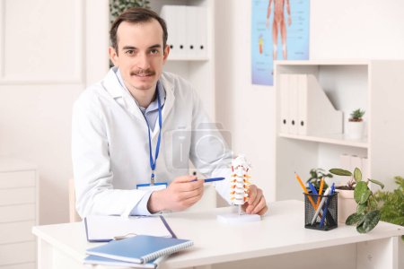 Médico varón demostrando anatomía espinal con modelo de columna vertebral en clínica