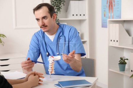 Médico masculino explicando anatomía espinal con modelo de columna vertebral al paciente en clínica