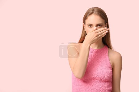 Mujer joven sintiendo terrible olor sobre fondo rosa