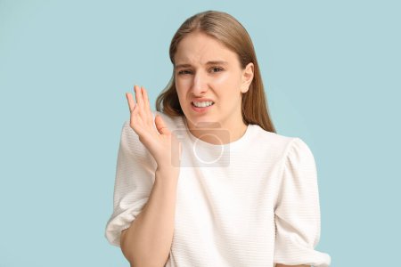 Young woman feeling bad smell on blue background