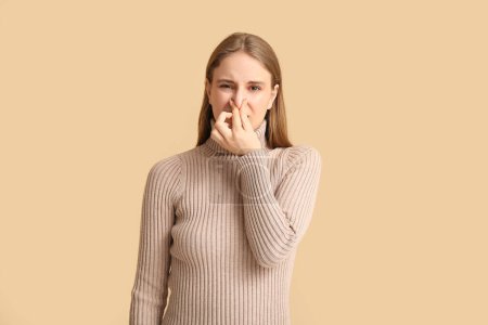 Photo for Young woman  pinching nose because of bad smell on beige background - Royalty Free Image